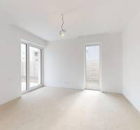 Prostorná místnost v rodinném domě s velkými okny a bílými stěnami.