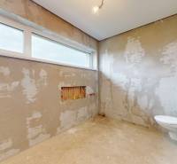 Neomítnutá koupelna s velkým oknem a sanitárním vybavením v rodinném domě.