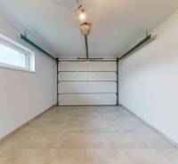 Garáž v rodinném domě s velkými vstupními vraty a oknem na boční stěně.