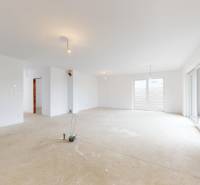 Interiér rodinného domu s bílými stěnami a velkými okny, podlaha připravená na úpravy.