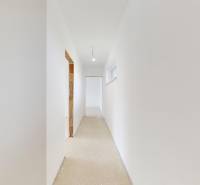 Bílá chodba v rodinném domě s nedokončenou podlahou a hladkými stěnami.