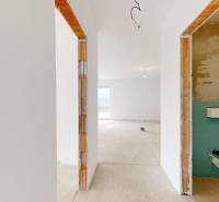 Ve výstavbě rodinného domu je světlá místnost s omítnutými stěnami a betonovou podlahou.