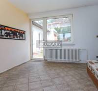 Interiér rodinného domu s dlaždicovou podlahou, sedačkou a velkým oknem.