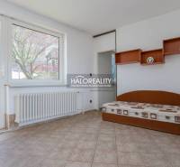 Interiér rodinného domu s postelí, poličkami, radiátorem a velkým oknem.