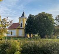 Kostel obklopený zelení v Práznovcích na zemědělských a lesních pozemcích.