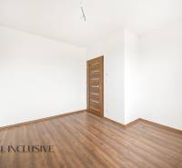 Prázdný pokoj v rodinném domě s bílými stěnami a podlahou s dřevěným dekorem.