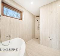 Koupelna v rodinném domě s vanou a sprchou, stěny mají mramorový vzhled.