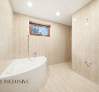 Koupelna s vanou a dlažbou v rodinném domě. Přírodní tóny a stylové osvětlení.