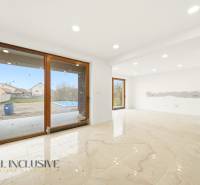 Prostorný interiér rodinného domu s velkými okny a výhledem na zahradu s bazénem.