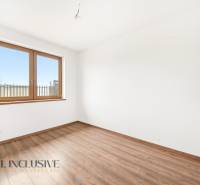 Pokoj v rodinném domě s bílými stěnami, dřevěným oknem a podlahou s dřevěným dekorem.