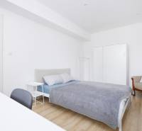 Ložnice dvoupokojového bytu s postelí, skříní a podlahou s dřevěným dekorem.