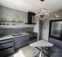 Kuchyně v 2-pokojovém bytě s betonovým vzhledem a geometrickým svítidlem.