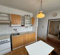 Kuchyně v 2-pokojovém bytě s kuchyňskou linkou, stolem, lavicí a podlahou s dřevěným dekorem.