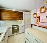 Kuchyně v rodinném domě s kuchyňskou linkou, závěsnými lampami a vestavěnými spotřebiči.