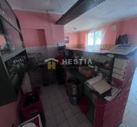 Interiér gastro prostorů s barovým pultem, pokladnou a sklenicemi na poličce.