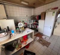 Kuchyně s gastro prostory, bílá dlažba, zásobníky, kuchyňské potřeby, ventilátor, ledničky.