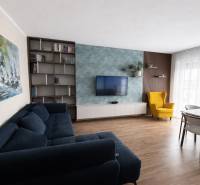 Obývací pokoj s modrou sedačkou, žlutým křeslem a podlahou s dřevěným dekorem ve 3-pokojovém bytě.