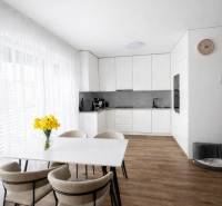 Jídelní stůl se židlemi a kuchyň v 3-pokojovém bytě s podlahou s dřevěným dekorem.