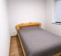 Ložnice v 2pokojovém bytě s postelí a podlahou s dřevěným dekorem.