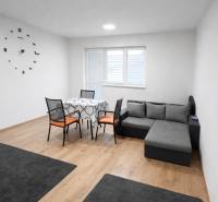 Obývací pokoj v 2-pokojovém bytě s pohovkou, stolem a podlahou s dřevěným dekorem.