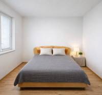 Světlá ložnice s podlahou s dřevěným dekorem v 2-pokojovém bytě, dekorovaná s postelí a lampou.