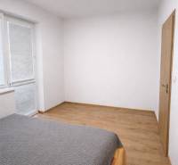 Ložnice v 2-pokojovém bytě s podlahou v dřevěném dekoru a velkým oknem.