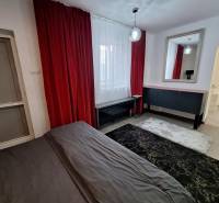 Interiér rodinného domu s červenými závěsy, zrcadlem a tmavým kobercem.