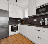 Kuchyně v 2-pokojovém bytě s podlahou s dřevěným dekorem, bílé skříňky, spotřebiče.