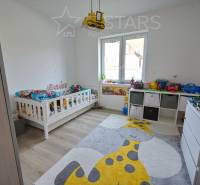 Dětský pokoj s postelí, hračkami, koberec s motivem žirafy, podlaha s dřevěným dekorem.