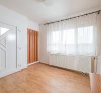 Interiér rodinného domu s bílými stěnami, okny a podlahou s dřevěným dekorem.