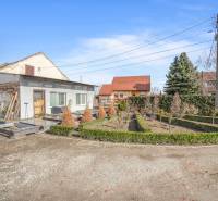 Obchodní prostory v Okoči s úpravou zahrady, obklopené stromy a keři.