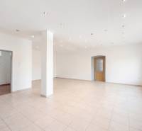 Prostorné obchodní prostory s bílými stěnami, dlažbou a rozsvícenými stropními světly.