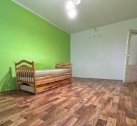 Pokoj s postelí v 2pokojovém bytě, podlaha s dřevěným dekorem, zelené stěny.
