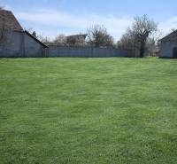 Zahrada v Dolní Seči obklopená rodinnými domy a oplocením pod modrou oblohou.