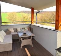 Prostorný balkon s ratanovým nábytkem a podlahou s dřevěným dekorem v garsonce.
