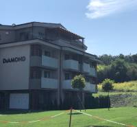 Budova 2-pokojového bytu v Podhájské obklopená zelení a bezoblačnou oblohou.