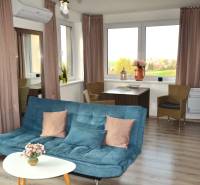 Obývací pokoj s pohovkou, stolkem, rostlinami a podlahou s dřevěným dekorem v 2pokojovém bytě.