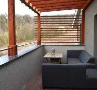 Balkon 2-pokojového bytu s dřevěným dekorem a výhledem na zeleň.