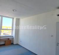 Interiér kanceláře s bílými stěnami, modrou podlahou a velkým oknem.