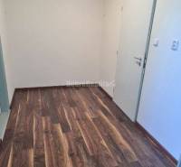 Chodba v kancelářích s podlahou s dřevěným dekorem a bílými stěnami.