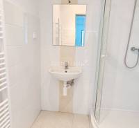 Koupelna s umyvadlem, sprchovým koutem a bílými obklady v kanceláři.