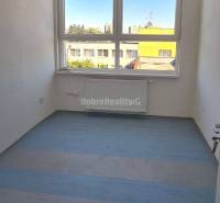 Místnost v kancelářích s velkým oknem, bílými stěnami a podlahou s dřevěným dekorem.