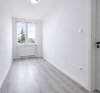 Úzká místnost s velkým oknem a podlahou s dřevěným dekorem ve 3-pokojovém bytě.