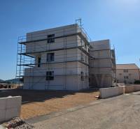 Stavební projekt ve městě Srima, obklopený lešením a pobřežním prostředím.