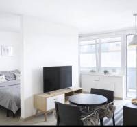 Světlý obývací pokoj v 2-pokojovém bytě s televizí a jídelním stolem.