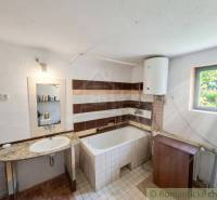 Koupelna v rodinném domě s umyvadlem, vanou a bojlerem.