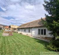 Rodinný dům v Ozdíně s původním vzhledem a travnatým dvorem, obklopený stromy.