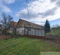 Rodinný dům v Ozdíně, obklopený zahradou a stromy, pod modrou oblohou.