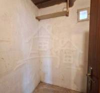 Malý pokoj s betonovou podlahou v rodinném domě, dřevěný strop, jednoduché stěny.