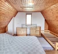 Podkrovní pokoj se střechou a stěnami obloženými dřevem, postel a komoda.